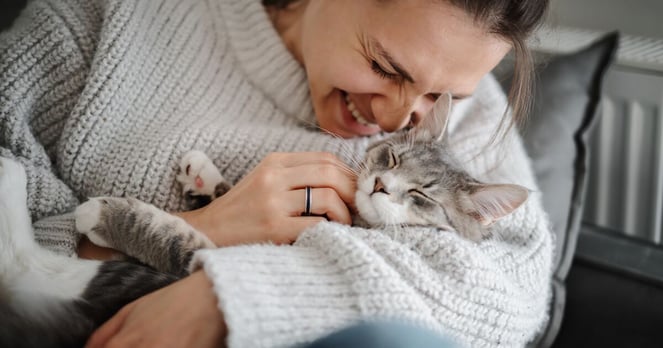 Woman cuddling her grey cat in her arms, smiling. 