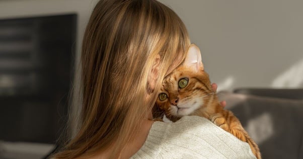 Woman facing away from the camera hugging her ginger cat who is looking over her shoulder.