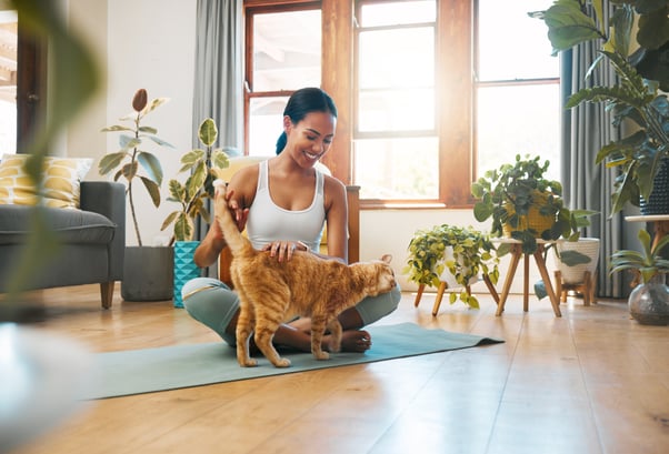 Smiling young woman on a yoga mat interacting with a ginger cat.