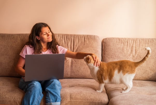 Young woman stroking a ginger and white cat on a sofa.