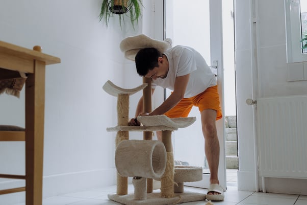Man standing on a tiled floor renovating a cat tree. 