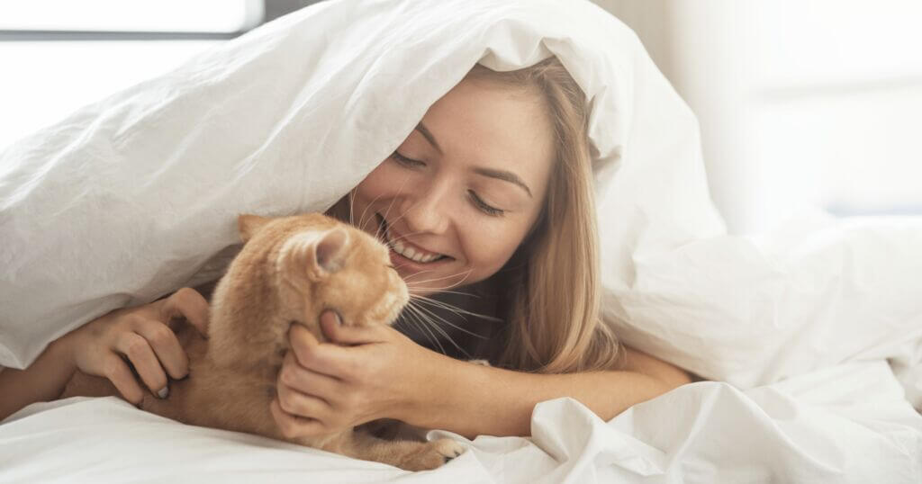 Woman laying in bed with duvet over her head petting cat