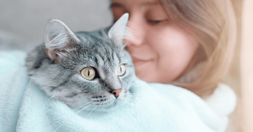 En kvinna håller en katt tätt intill sig och ser lugn och trygg ut